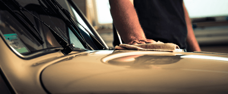 A hand cleaning the hood of a car